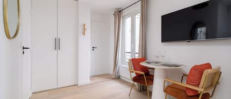 Un comedor moderno con una mesa blanca, dos sillas y un televisor de pantalla plana montado en la pared.