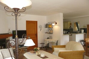 A living room with a fireplace, a television, a dining area with a table and chairs, and a kitchen in the background. - Holiday home in Cogolin with swimming pool (Cogolin)