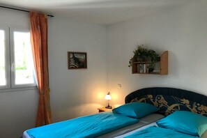 A bedroom with a bed, a nightstand with a lamp, a window with curtains, a wall-mounted shelf with books and a plant, and a framed picture on the wall. - Holiday home in Cogolin with swimming pool (Cogolin)