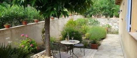 Eine Terrass mit Tisch und Stühlen, umgeben von Blumentöpfen und einer Steinmauer.