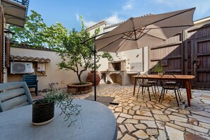 Un patio esterno con un tavolo rotondo e sedie, un ombrellone grande e un pavimento in pietra.