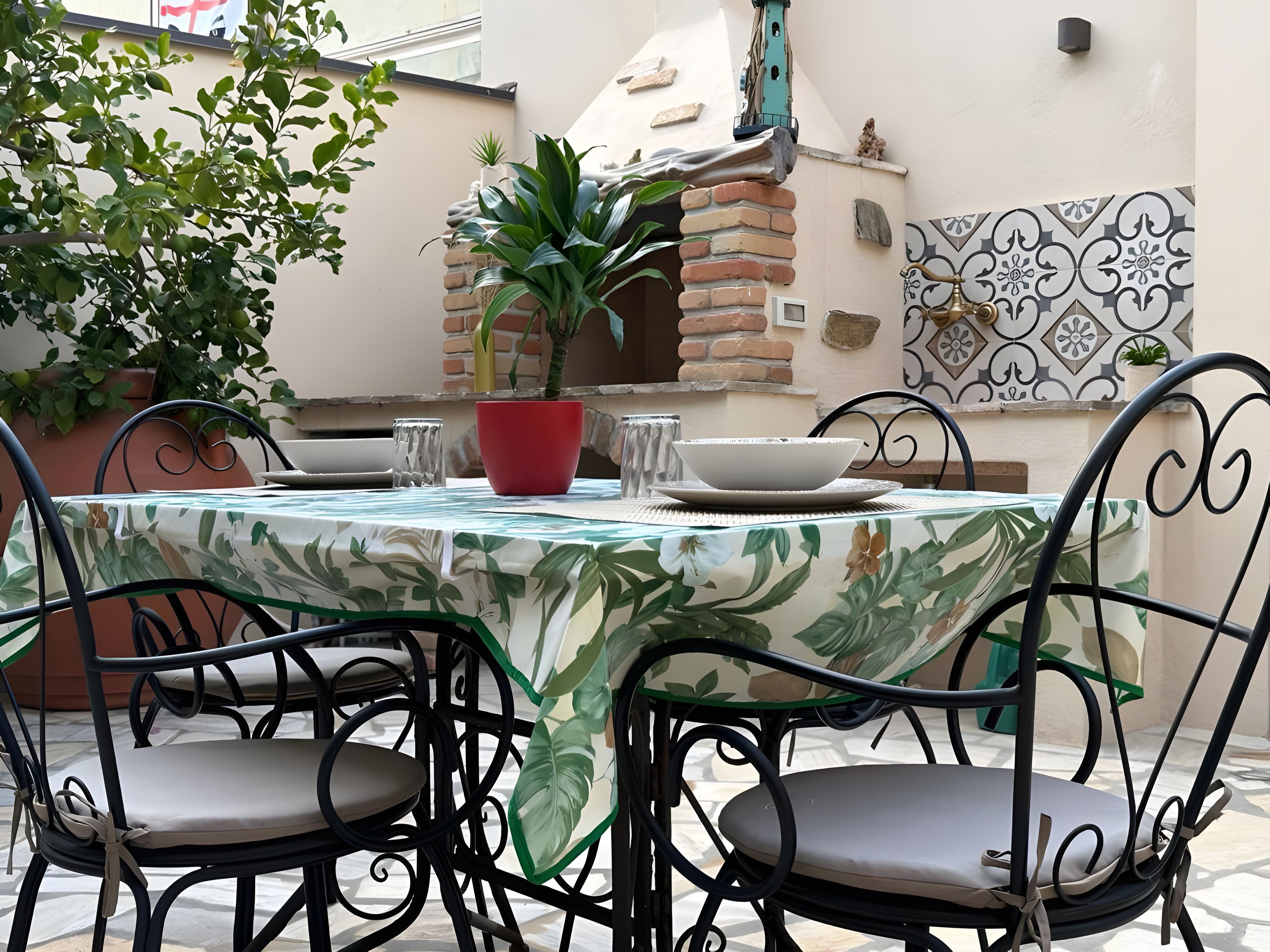 An outdoor patio with a round table, chairs, a potted plant, and a brick oven.