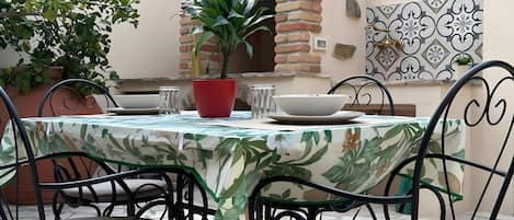 An outdoor patio with a round table, chairs, a potted plant, and a brick oven.