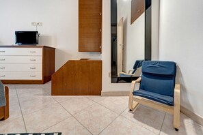 A room with a wooden cabinet, a television on top, a blue chair, and a mirror reflecting a staircase. - Angela House Teulada – Comfort and Relaxation in the Heart of Southern Sardinia (Teulada)