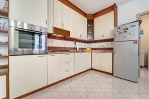 Eine Küche mit weißen Schränken, einem Edelstahlbackofen, einem gelben Wasserkocher und einem Kühlschrank mit Magneten.
