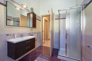 Un bagno moderno con cabina doccia in vetro, un lavabo con specchio e pavimento piastrellato.