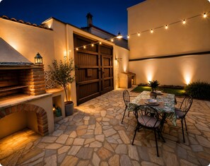 Un patio esterno con pavimento in pietra, un forno a mattoni, un tavolo apparecchiato per consumare pasti e luci decorative a catena.