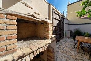 Ein Backsteinbau, ein Holztisch mit Stühlen und eine mit Steinplatten belegte Terrasse.