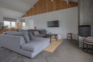 A modern living room with a grey sectional sofa, a flat-screen TV mounted on the wall, and a fireplace. - Holiday home with 1 bedroom (Cadzand-Bad)