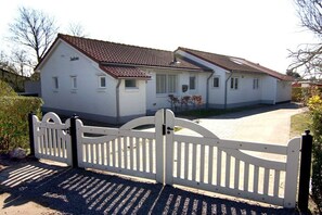A two-story white building with a brown roof, a gated driveway, and a small garden area. - Holiday home with 1 bedroom (Cadzand-Bad)