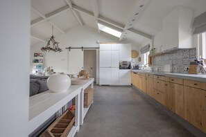 A modern kitchen with white cabinetry, a central island, and a dining area with a sofa and cushions. - Holiday home with 1 bedroom (Cadzand-Bad)