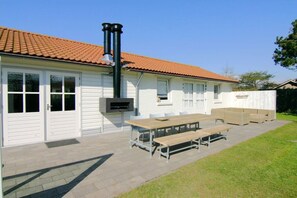 A house with a tiled roof, a barbecue grill, and a patio with a table and benches. - Holiday home with 1 bedroom (Cadzand-Bad)