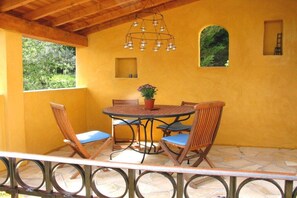 Eine überdachte Terrasse mit einem runden Tisch, vier Stühlen und einer hängenden Leuchte.