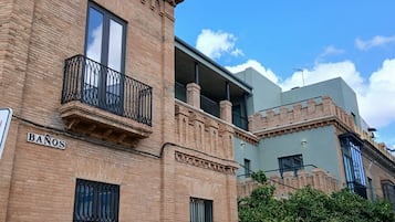Un bâtiment en briques doté d’un balcon, une enseigne indiquant « BANOS », et une structure moderne en arrière-plan.