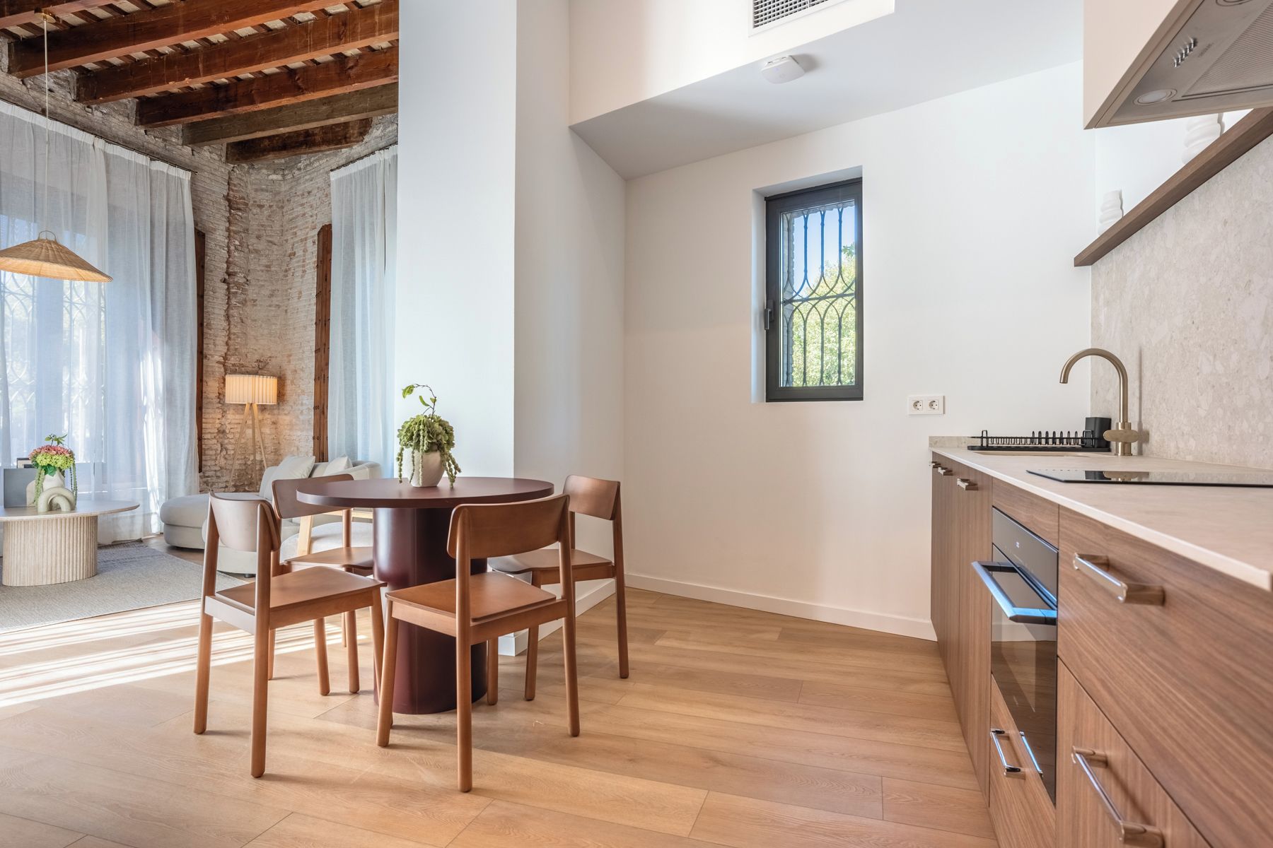 A modern kitchen with wooden cabinets, a round dining table with chairs, and a window with a metal grill.