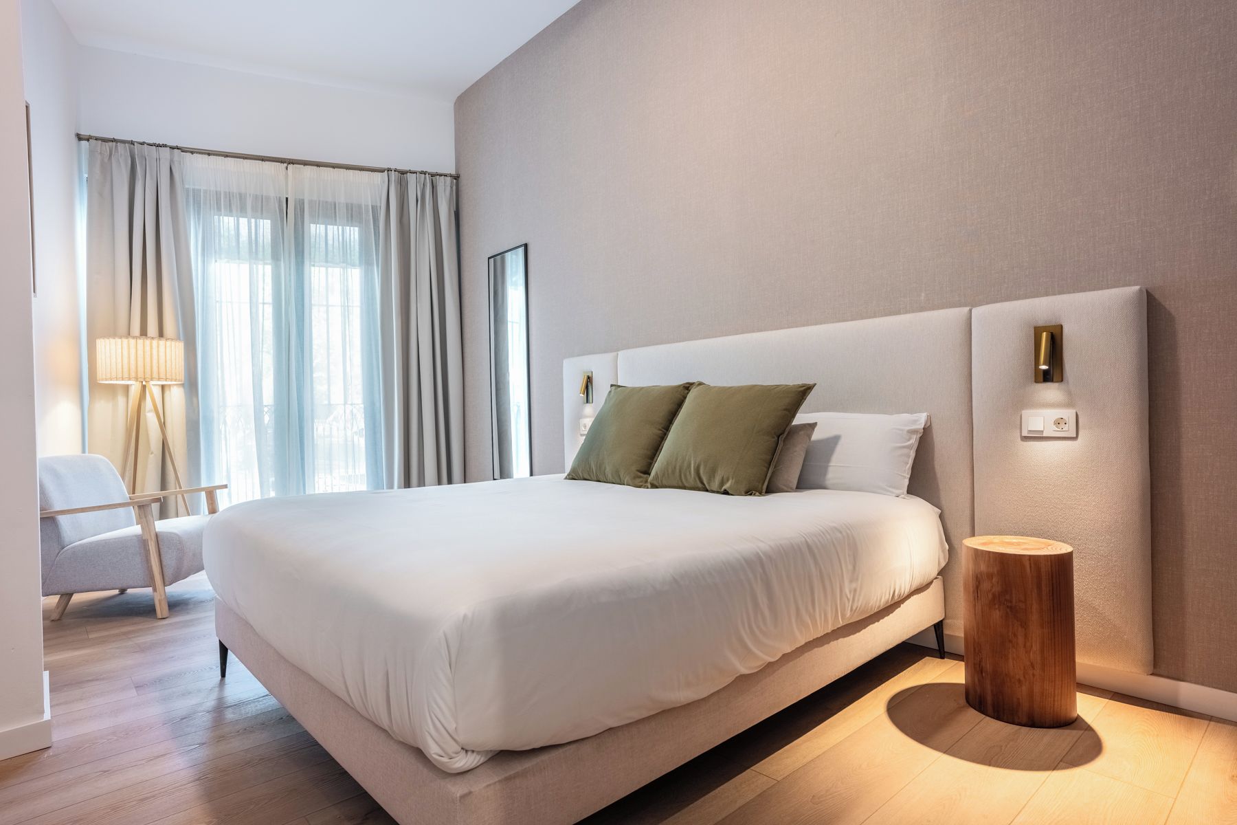 A modern hotel room with a large bed, a bedside table, a lamp, and a chair.