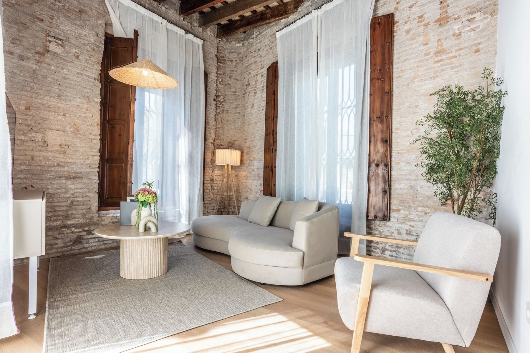 Une pièce aux murs en briques apparentes, avec une table basse ronde, un canapé, un fauteuil et une plante en pot.