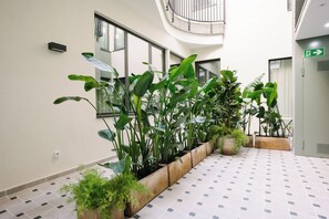 Un pasillo con plantas en macetas, suelo de baldosas y una escalera al fondo.