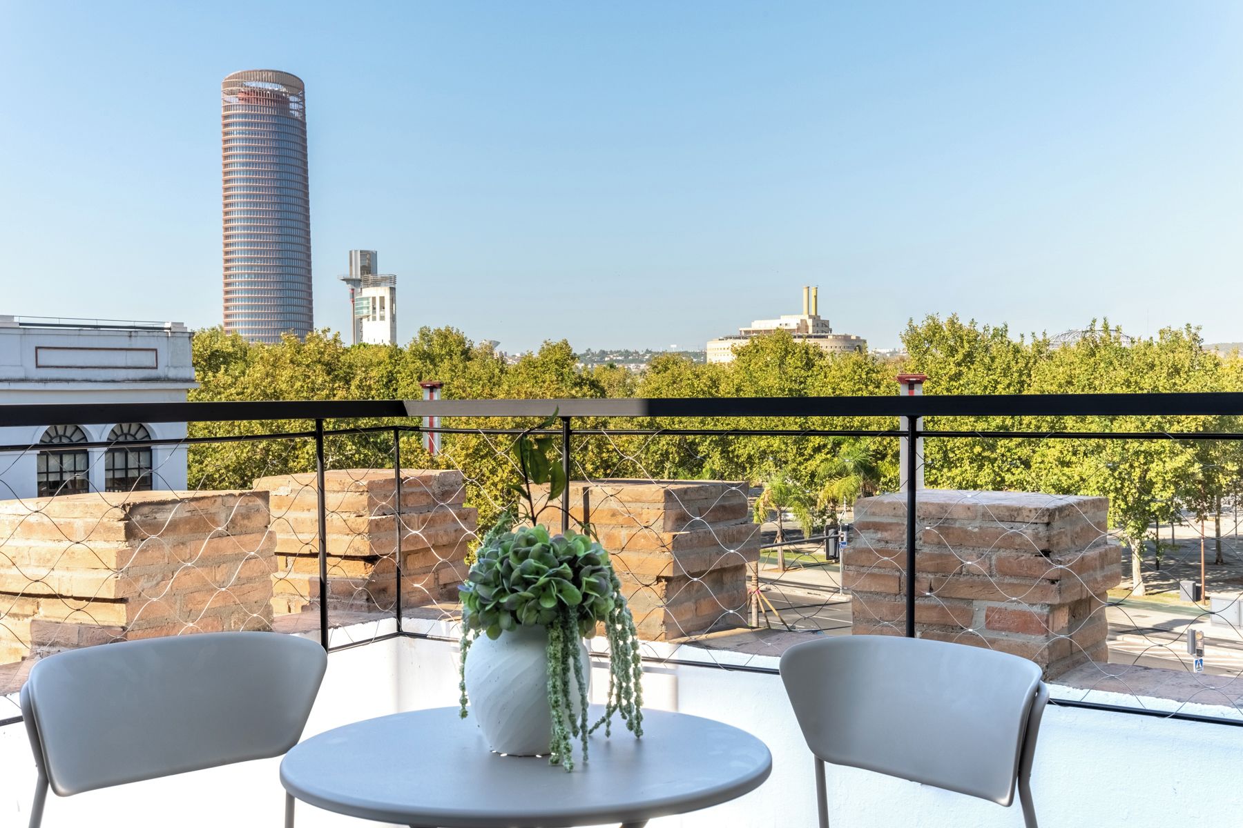 A rooftop terrace with a table and chairs, a potted plant, and a view of the city skyline.