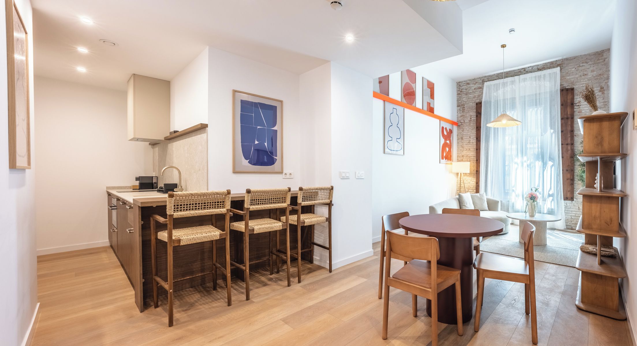 A modern kitchen with a dining area, wooden furniture, and artwork on the walls.