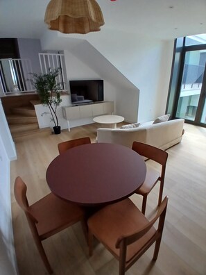 Ein modernes Wohnzimmer mit rundem Tisch, Stühlen, einer Couch, einem Fernseher und einer Treppe.