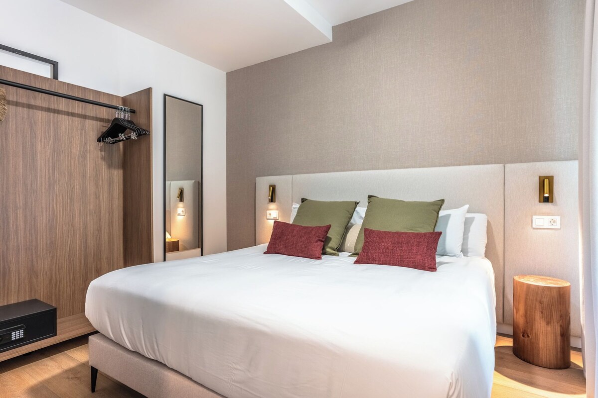Una habitación de hotel moderna con una cama grande, lámparas de noche, un armario y una mesita de noche.
