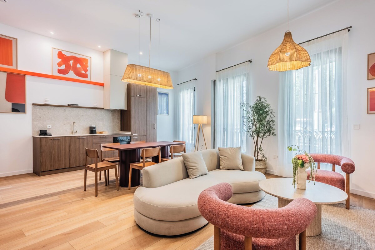Una sala de estar moderna con un sofá, sillas, una mesa de comedor y una zona de cocina con armarios y una encimera.