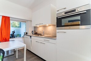 Eine moderne Küche mit weißen Schränken, einem eingebauten Backofen und einem Fenster mit orangefarbenen Vorhängen.