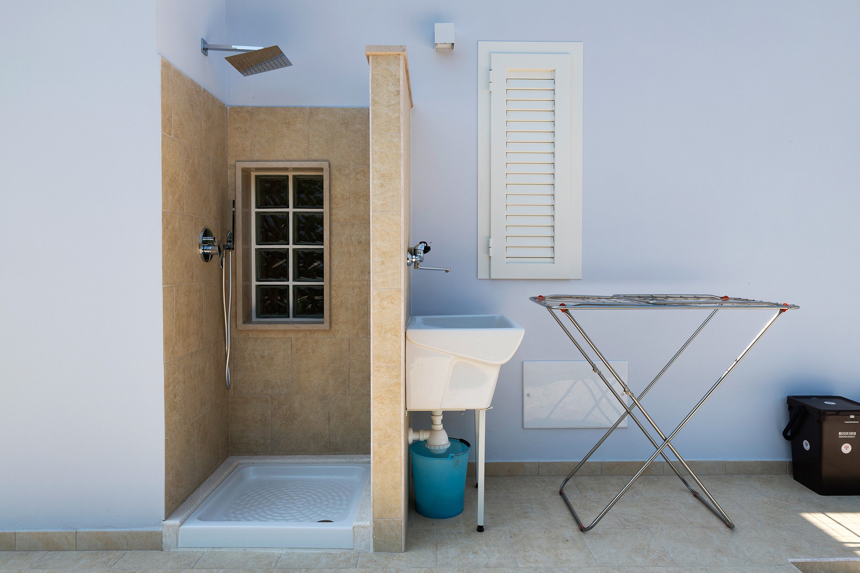 Un bagno con doccia, lavandino, una finestra con persiane e uno stendibiancheria.