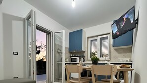 Cozinha moderna com área de refeições, uma TV de tela plana montada acima do balcão e uma porta de vidro deslizante para área externa.