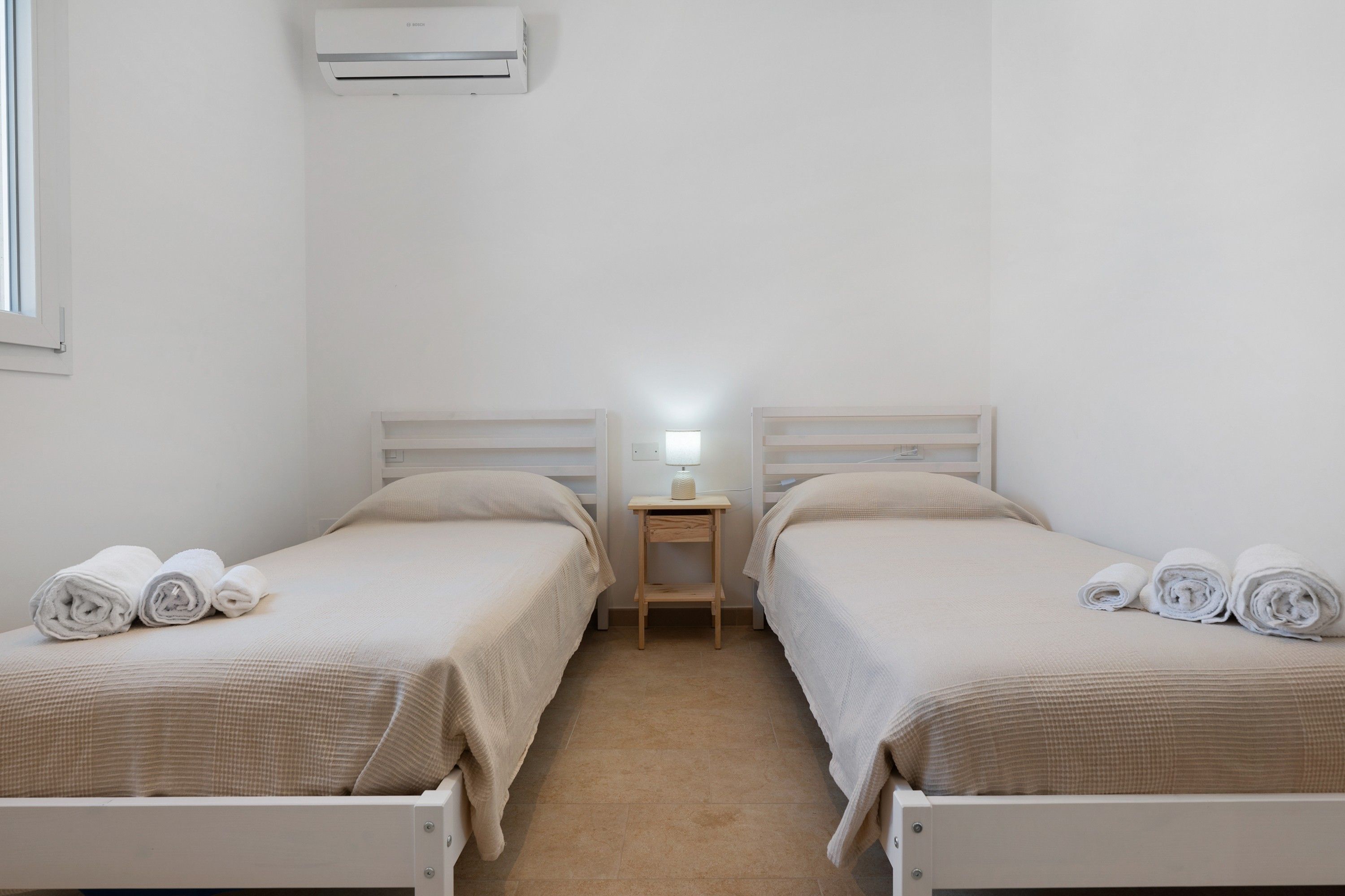 Ein Hotelzimmer mit zwei Betten, einem Nachttisch mit Lampe und einer Klimaanlage an der Wand.