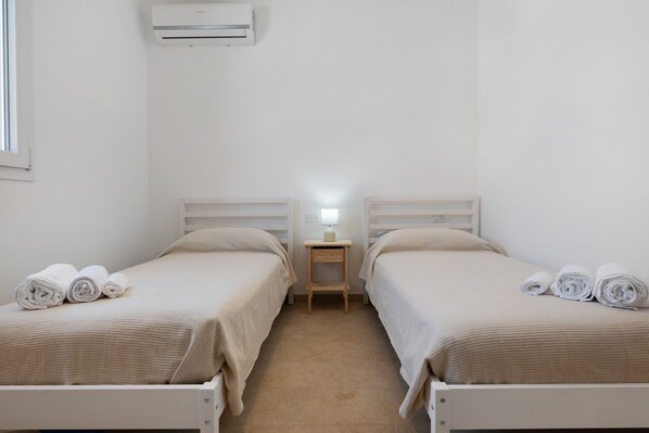 A hotel room with two beds, a nightstand with a lamp, and an air conditioning unit on the wall.