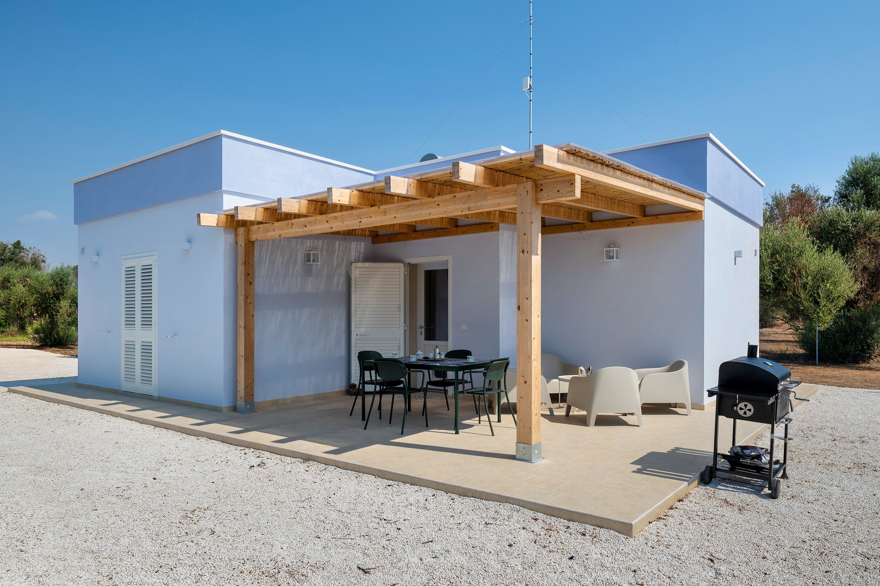 Un petit bâtiment d’un seul étage, doté d’un patio couvert, d’une table avec des chaises et d’un barbecue.