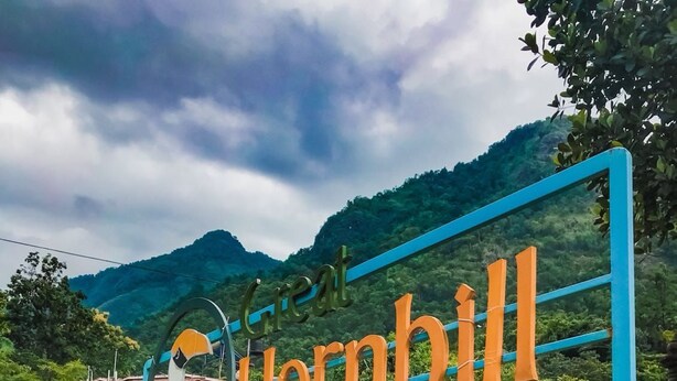Een bord met de naam 'Hornbill' in grote letters, omringd door weelderige begroeiing en heuvels op de achtergrond.
