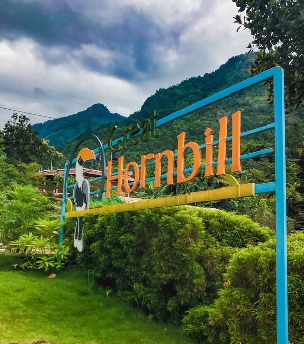 Une enseigne portant le nom « Hornbill » en grandes lettres, entourée d’une végétation luxuriante et avec des collines en arrière-plan.
