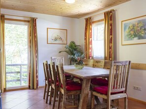 A dining area with a wooden table and chairs, a potted plant, and a painting on the wall. - Cabin in Annaberg With Swimming Pool (Annaberg-Lungoetz)