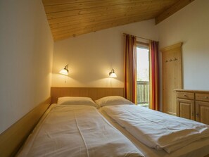 A room with two beds, wooden headboard, wall-mounted lamps, a window with curtains, and a wooden wardrobe. - Cabin in Annaberg With Swimming Pool (Annaberg-Lungoetz)