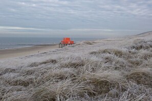 A beach with a red lifeguard tower on a pier. - Holiday home with 1 bedroom (Callantsoog)
