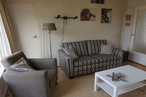 A living room with a striped sofa, a grey armchair, a white coffee table, and a floor lamp. - Holiday home with 1 bedroom (Callantsoog)