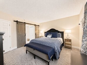 A bedroom with a bed, bedside tables, a bench, and a wardrobe with a sliding door. - Riverfront Retreat | Balcony + Pool | Heart of Pigeon Forge | FREE Dollywood (Pigeon Forge)