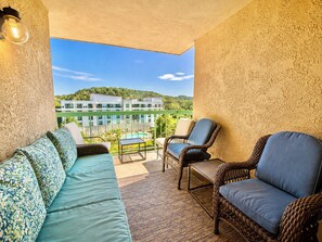 Ein Balkon mit einer Couch, Stühlen und einem Tisch. Im Hintergrund ist ein Gebäude mit einem Pool zu sehen.