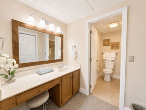 Een badkamer met een houten wastafelmeubel, een grote spiegel en een toilet dat door een geopende deur zichtbaar is.