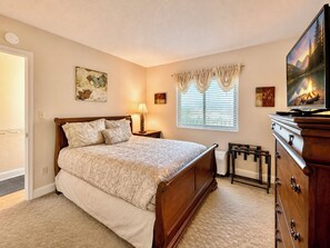 Een slaapkamer met een bed, een dressoir, een televisie en een raam met gordijnen.