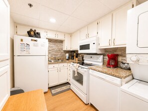 A compact kitchen with white cabinets, a microwave, an oven, a coffee maker, and a dishwasher. - Riverfront Retreat | Balcony + Pool | Heart of Pigeon Forge | FREE Dollywood (Pigeon Forge)
