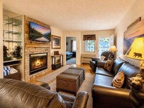 A cozy living room with a fireplace, leather sofas, and a television mounted on a stone wall. - Riverfront Retreat | Balcony + Pool | Heart of Pigeon Forge | FREE Dollywood (Pigeon Forge)