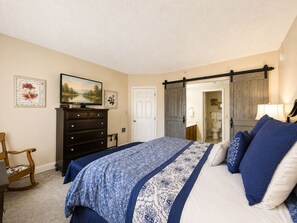 Ein Schlafzimmer mit Bett, Kommode, Fernseher und einer Tür zu einem Badezimmer.