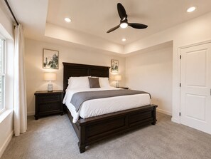 A bedroom with a dark wood bed, two bedside tables with lamps, a ceiling fan, and a door. - New Pige Forge Condo | Walk Everywhere (Pigeon Forge)
