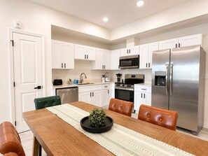 A modern kitchen with white cabinets, stainless steel appliances, and a wooden dining table with chairs. - New Pige Forge Condo | Walk Everywhere (Pigeon Forge)