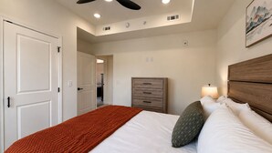A bedroom with a bed, a dresser, a ceiling fan, and a nightstand with a lamp. - New Pige Forge Condo | Mtn View - Walk Everywhere (Pigeon Forge)