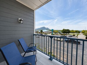 A balcony with two chairs, a view of a parking lot, and a mountain in the distance. - New Pige Forge Condo | Walk Everywhere (Pigeon Forge)